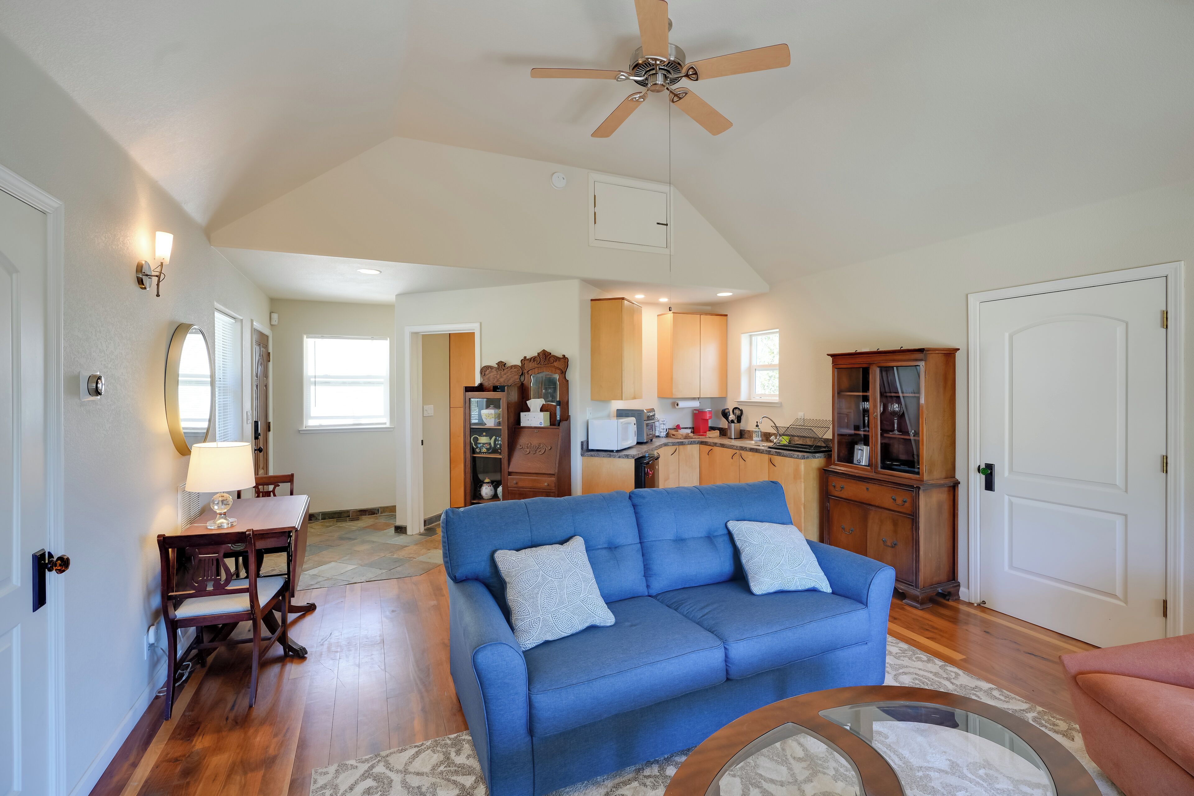 A spacious living room with a blue sofa, wooden dining table, and a ceiling fan.
