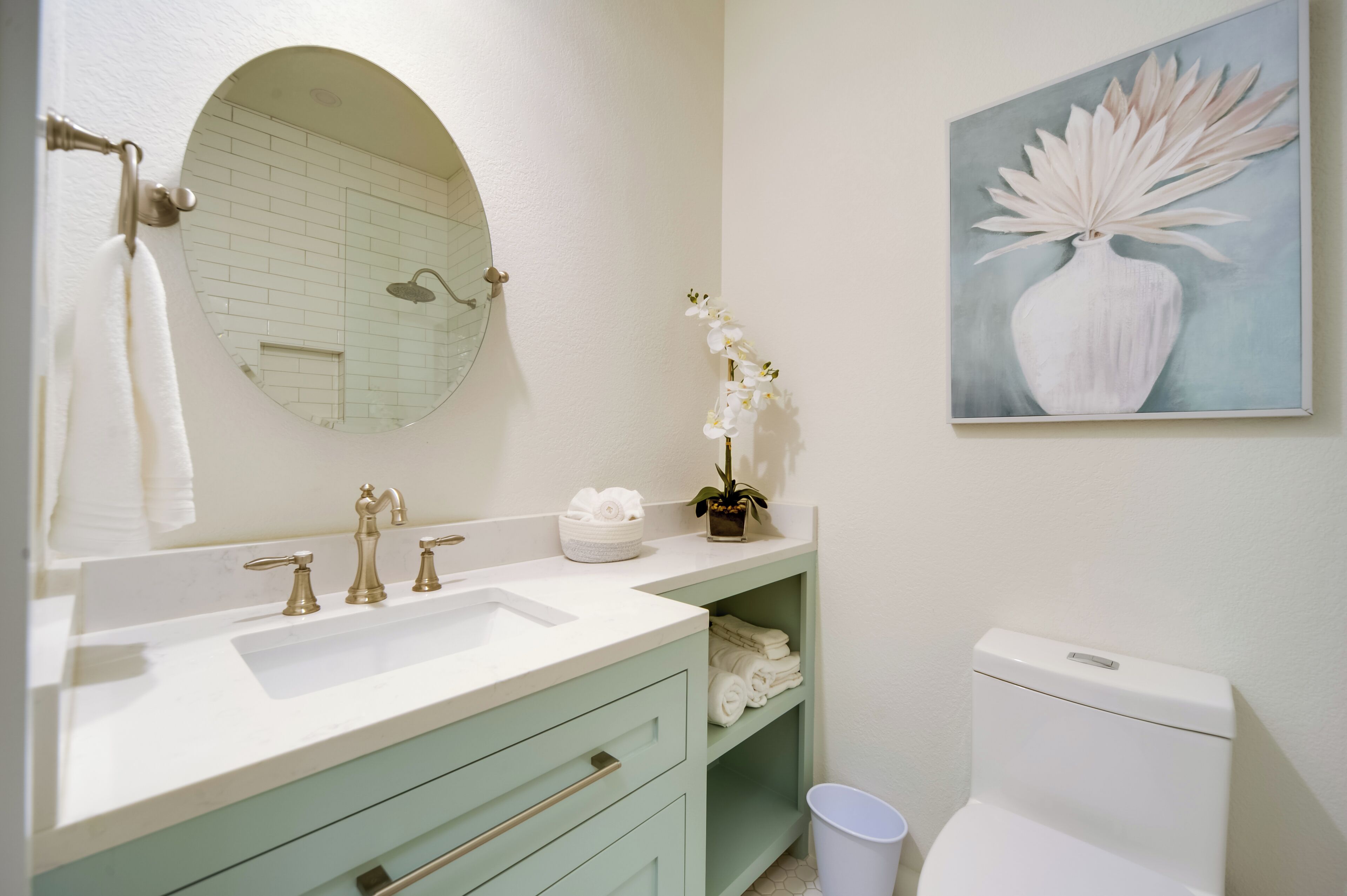 Une salle de bain avec un lavabo blanc, deux robinets, un miroir, des toilettes et une étagère avec des serviettes.