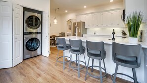 A modern kitchen with white cabinets, a built-in washing machine, and a bar area with stools. - Cocktail Pool! Fredericksburg Bungalow By Main St (Fredericksburg)