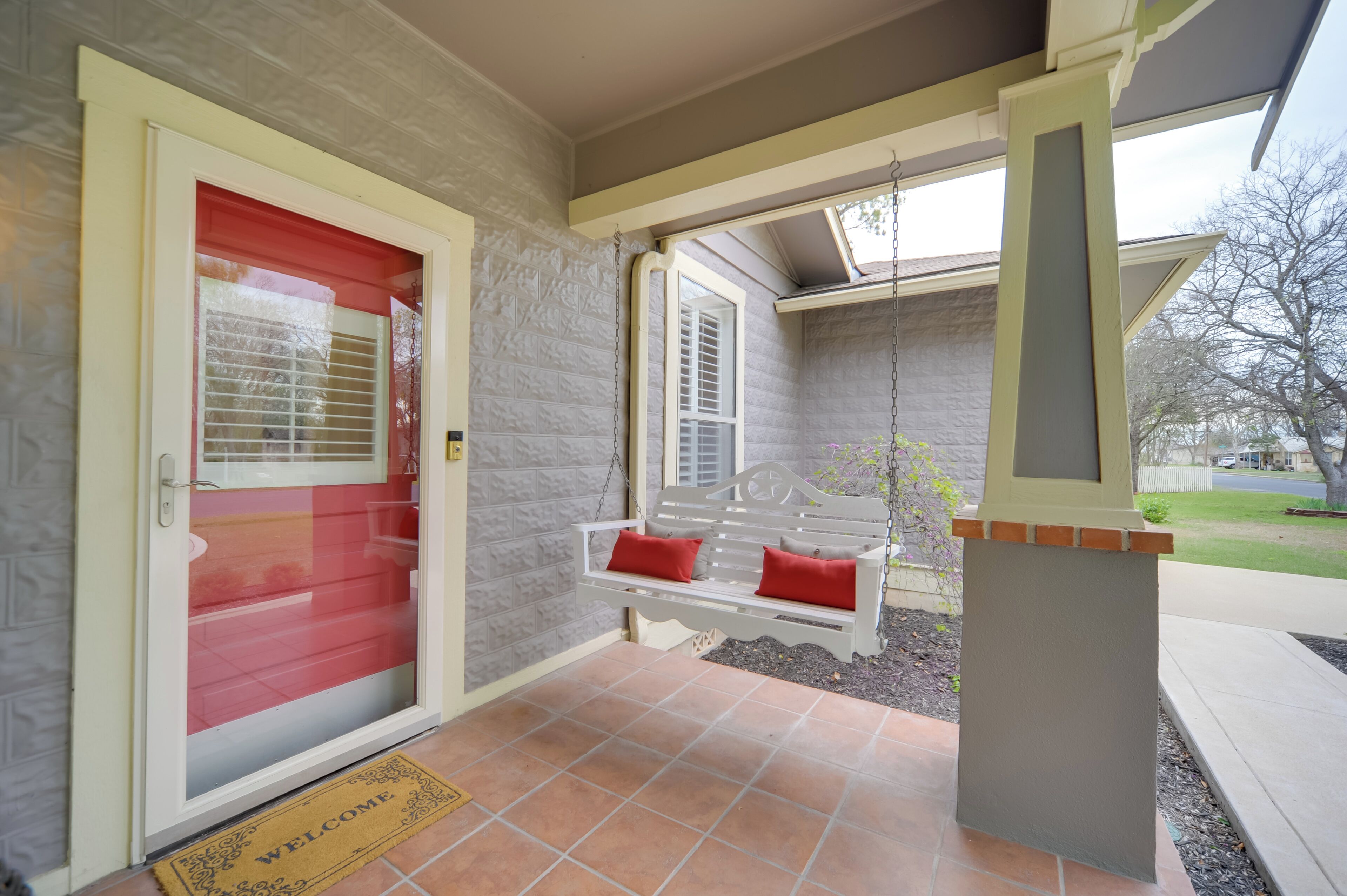 A front porch with a red door, a white bench with red cushions, and a welcome mat.