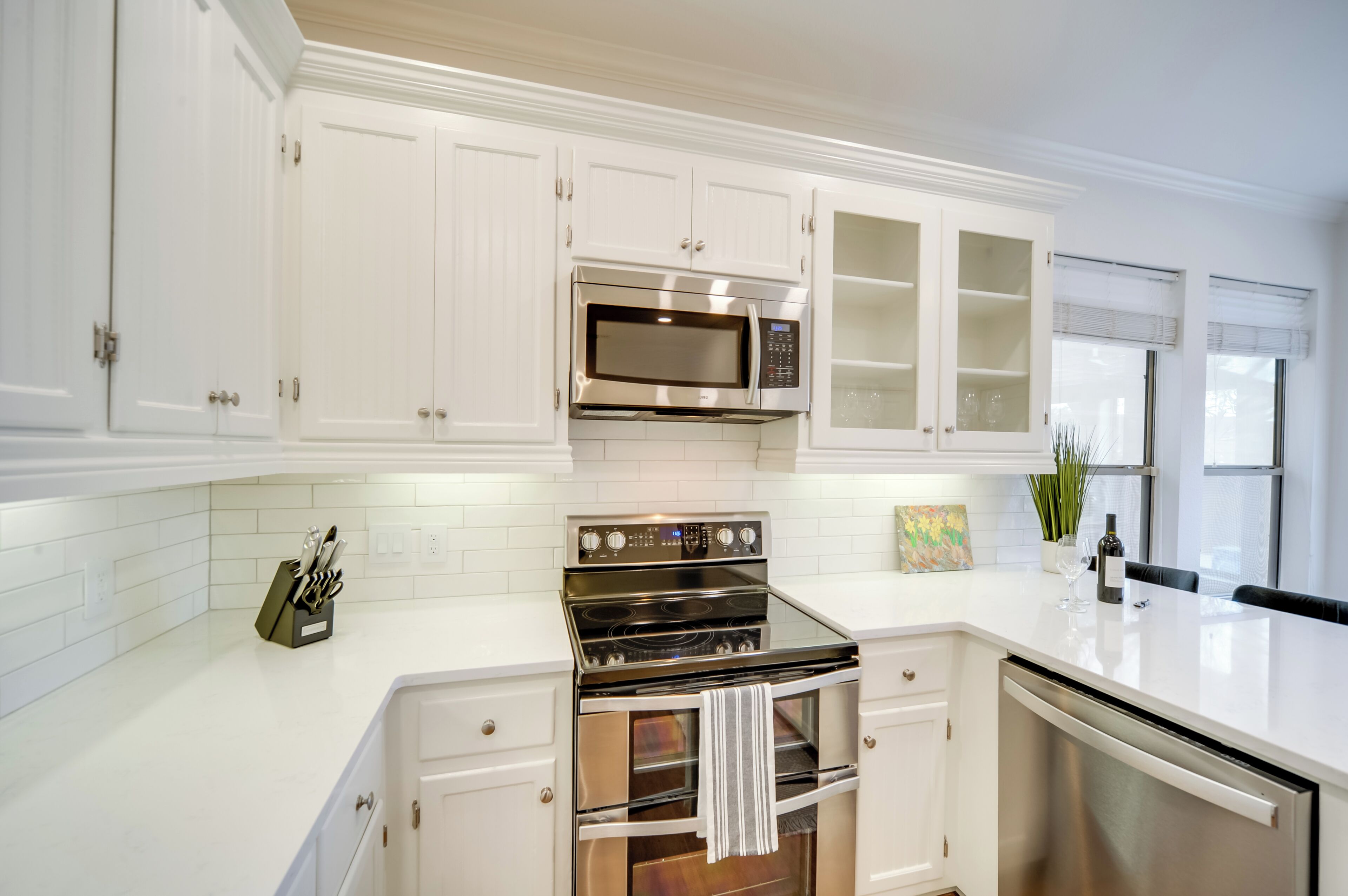 Una cocina moderna con armarios blancos, electrodomésticos de acero inoxidable y una encimera blanca.