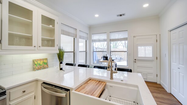 A modern kitchen with white cabinetry, a large island with a wooden countertop, and a view of the backyard through large windows. - Cocktail Pool! Fredericksburg Bungalow By Main St (Fredericksburg)