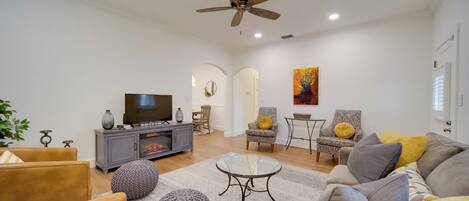 A modern living room with a television, sofa, armchairs, and a glass coffee table.