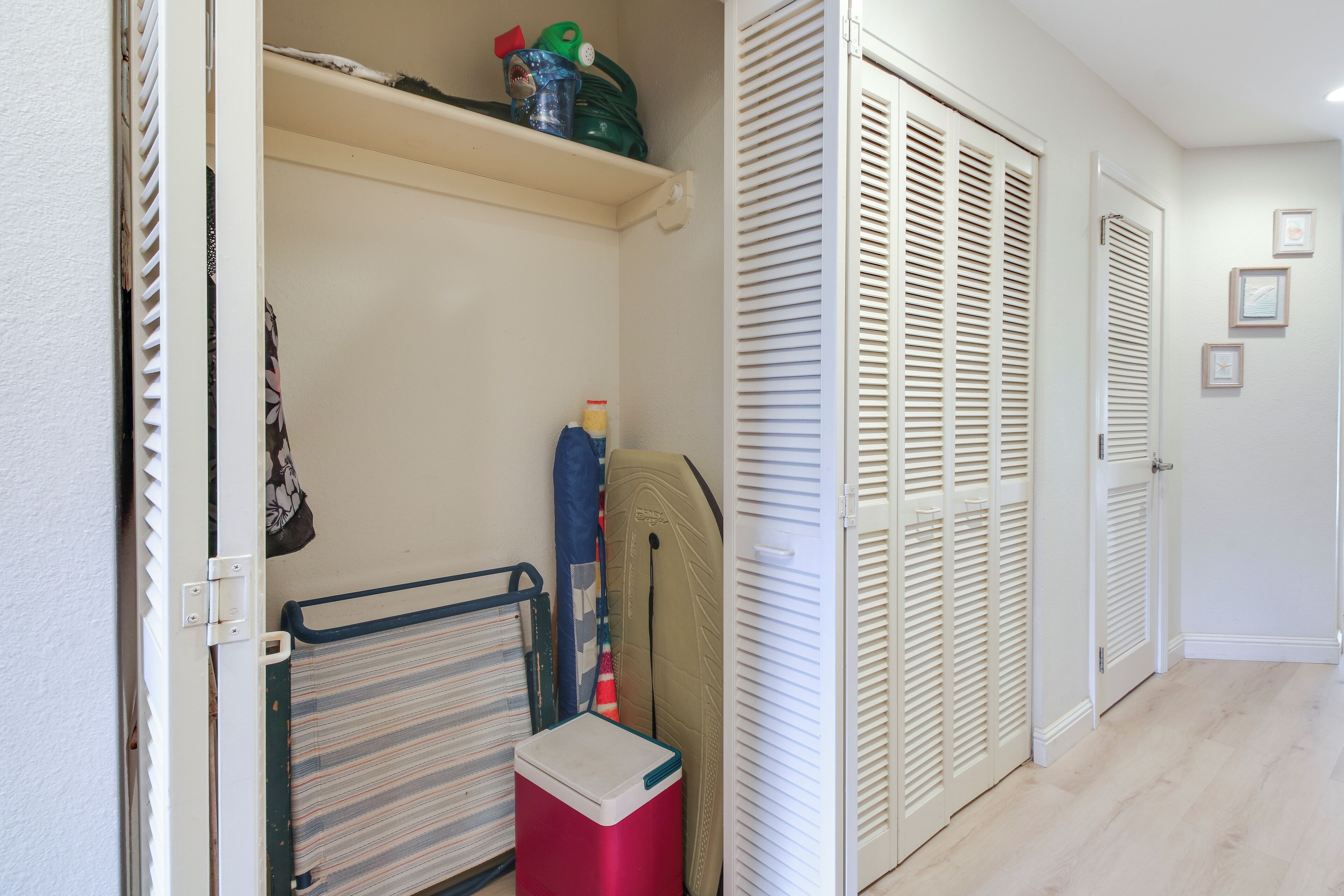 A hallway with a storage unit, a red cooler, and a surfboard leaning against the wall.