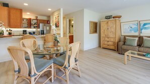 Eine moderne Küche mit Holzausstattung, ein Essbereich mit Korbstühlen und ein Wohnzimmer mit Sofa und Couchtisch.