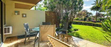An outdoor patio with a wooden bench, two chairs, and a table.