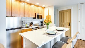 Een moderne keuken met houten kastjes, een centraal eiland en een eethoek met twee stoelen.