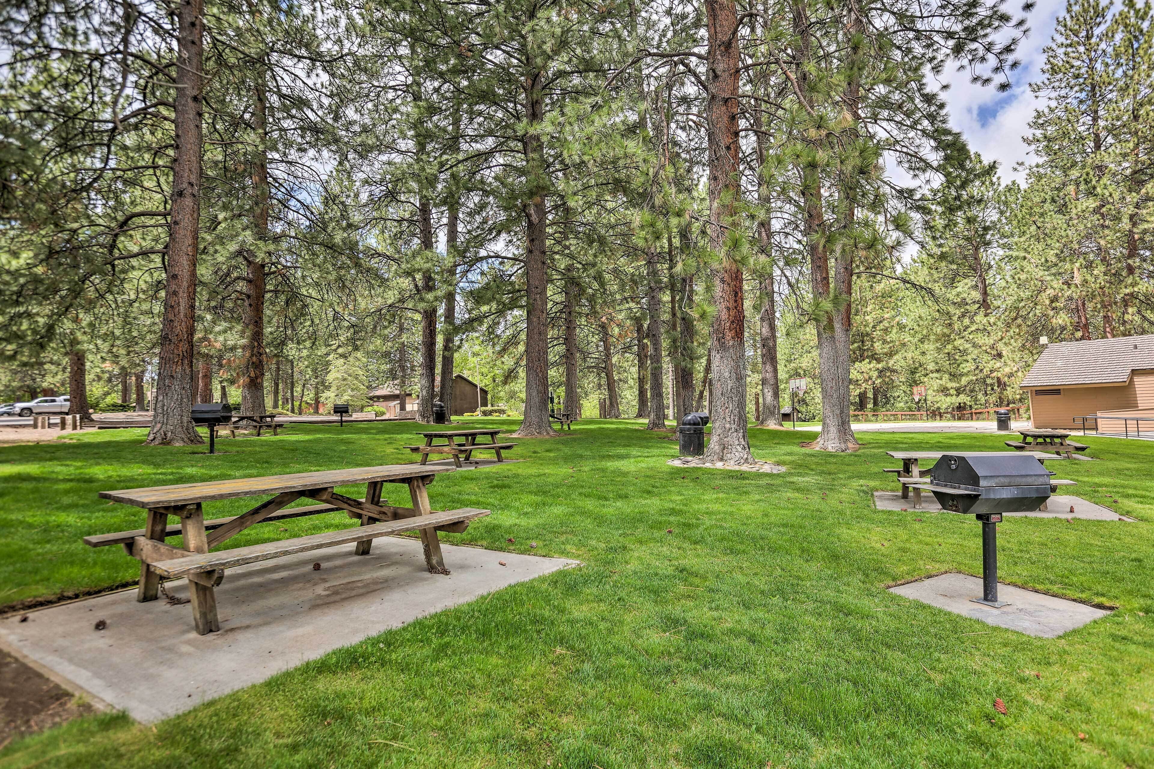 A picnic area with picnic tables and a barbecue grill surrounded by tall trees.