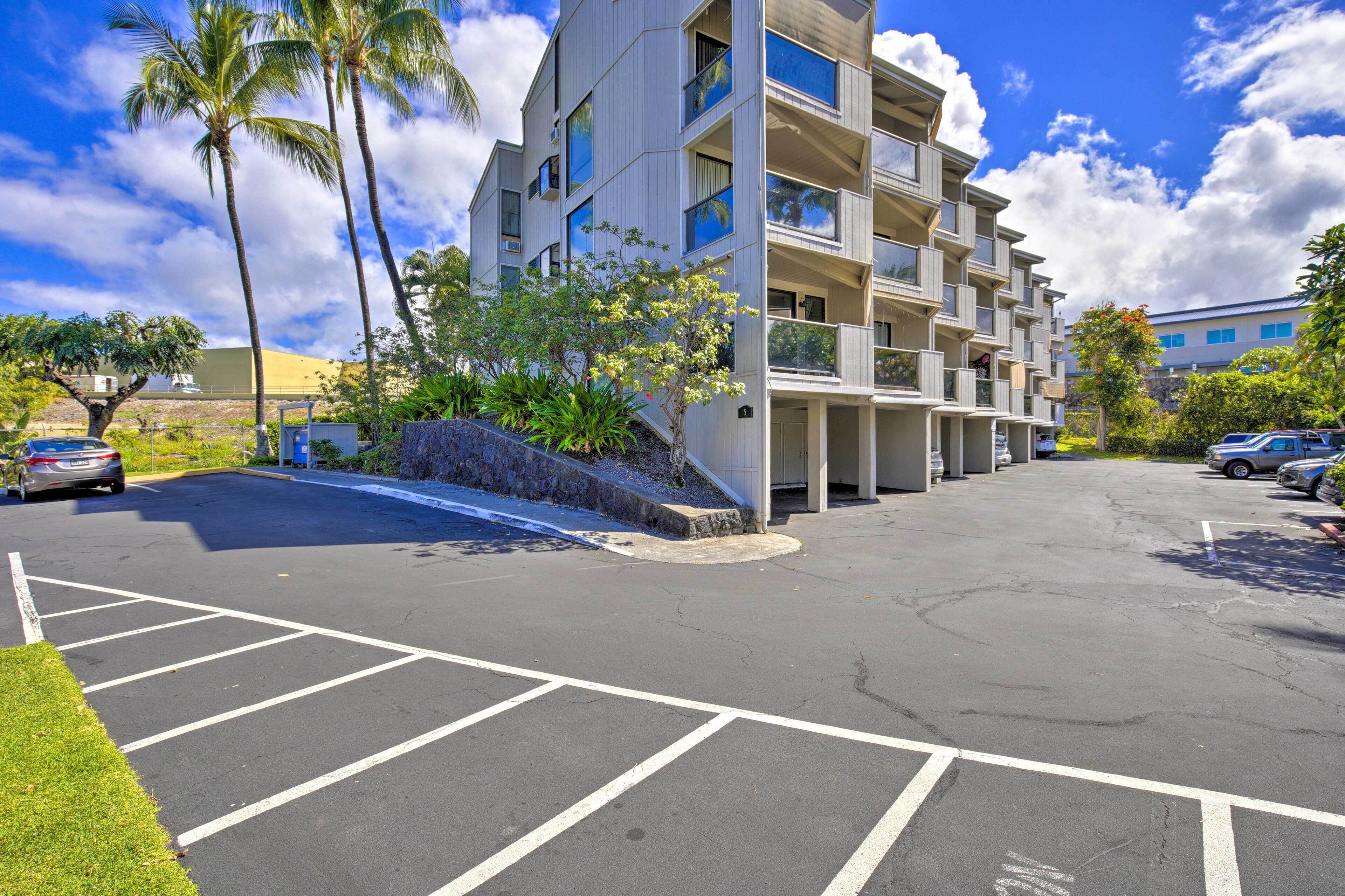 A multi-story parking garage with clear markings for parking spaces, surrounded by palm trees and a building with balconies.