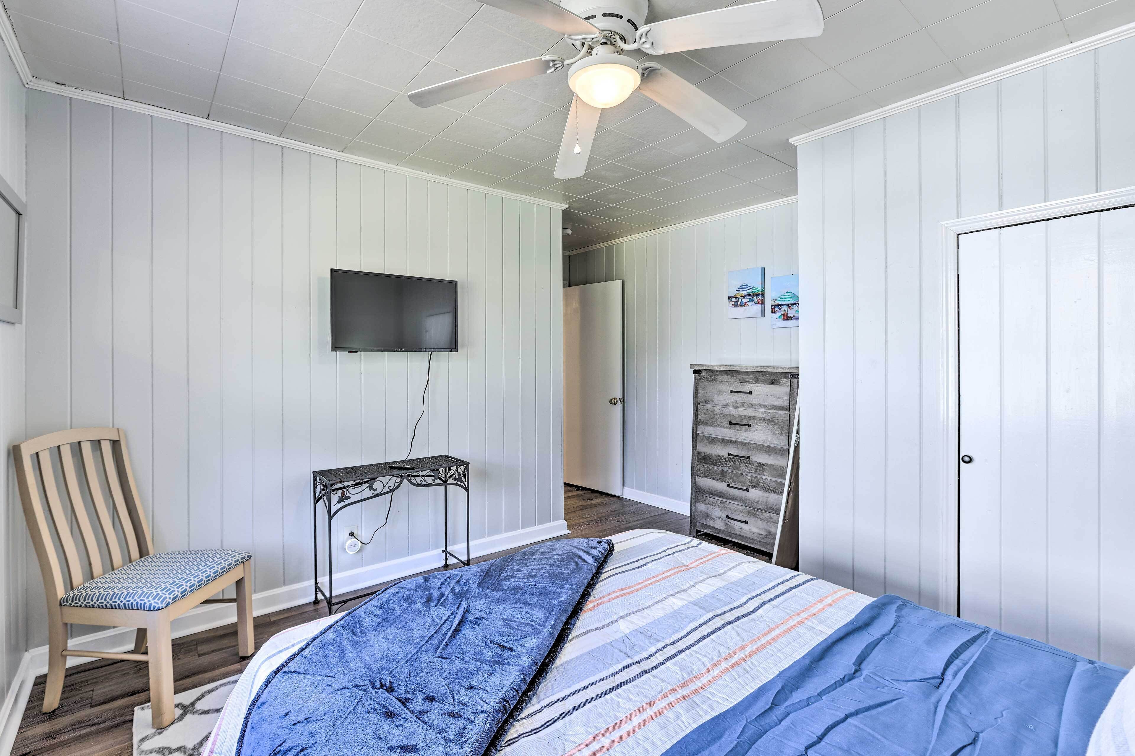 A bedroom with a bed, a chair, a desk, a wardrobe, and a ceiling fan.
