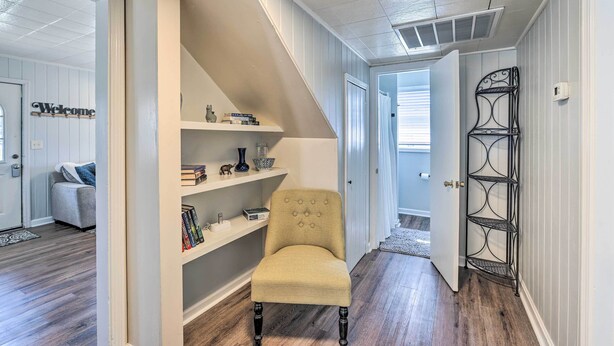A hallway with a beige armchair, white shelves with decorative items, and a metal rack. - Tuscaloosa House 2 Mi to Coleman Coliseum! (Tuscaloosa)