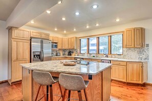 Una cocina moderna con armarios de madera, un refrigerador de acero inoxidable, encimeras de granito y un amplio ventanal que proporciona luz natural.