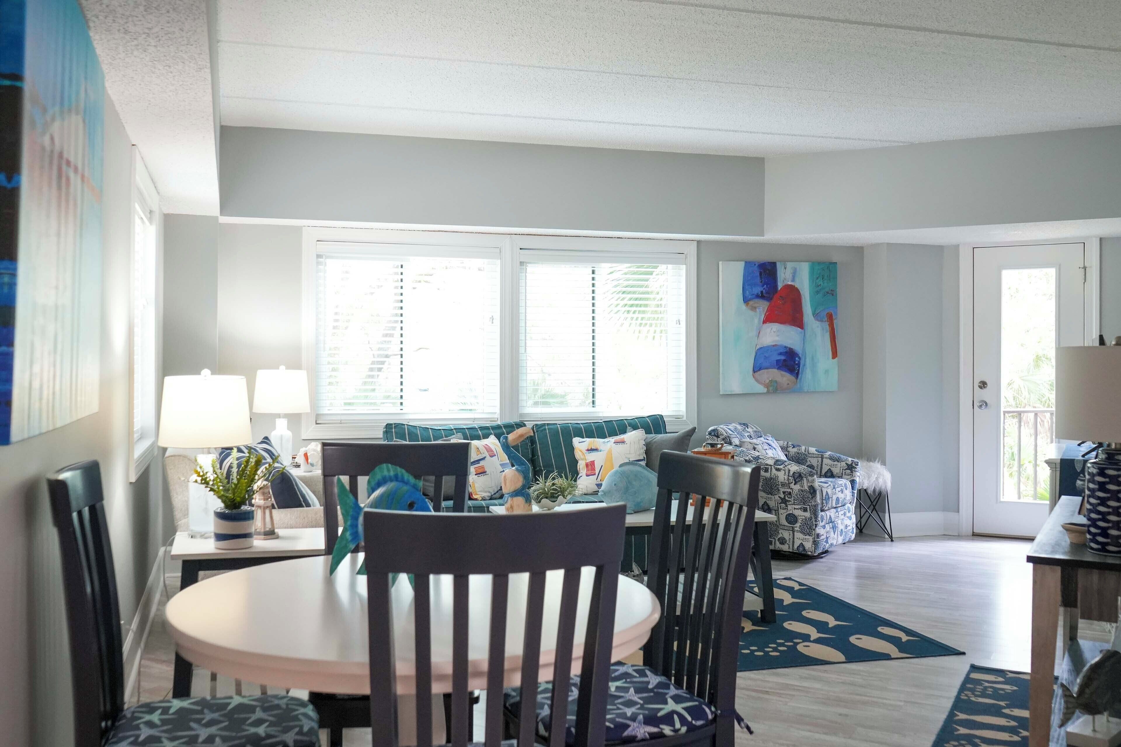 A dining area with a round table, chairs, and a sofa with patterned cushions.