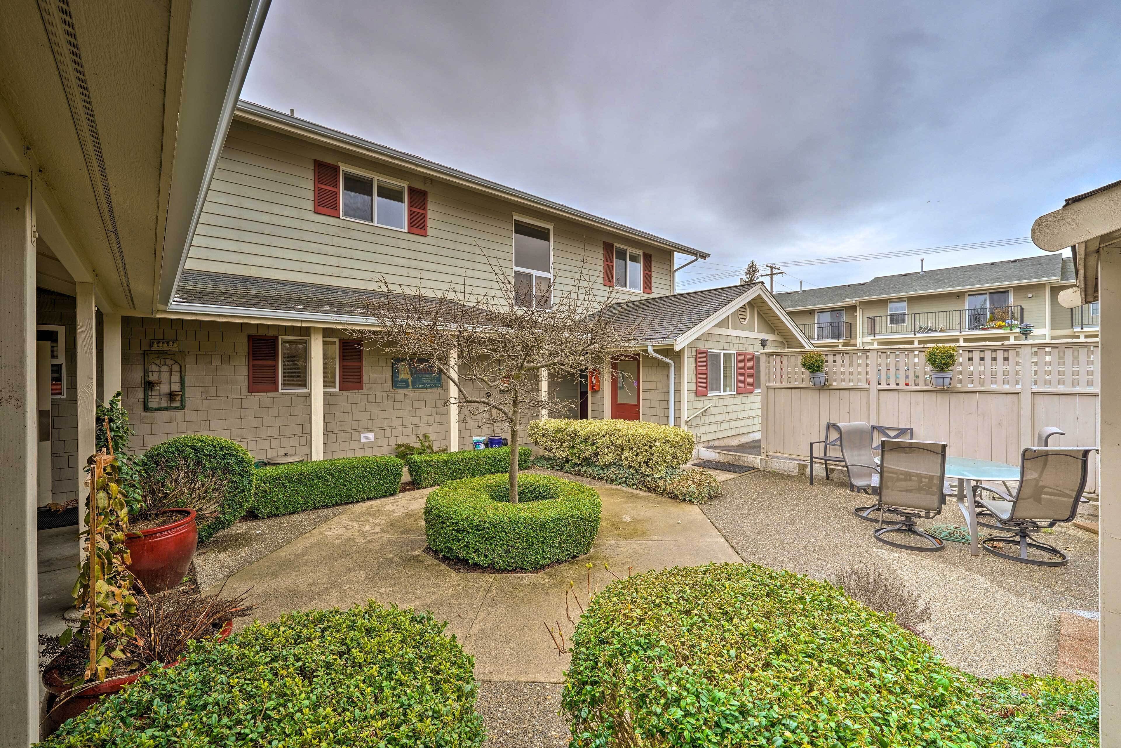A residential building with a covered patio area, outdoor seating, and a small tree.