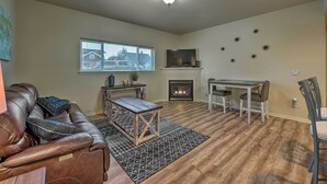 A living room with a leather couch, a wooden coffee table, a fireplace, a dining table with chairs, and a TV mounted on the wall. - Central Apt: Private Fireplace & Patio Access (Anacortes)