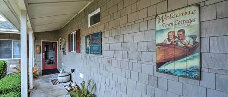 A covered walkway with a brick wall, a welcome sign for town cottages, and a sign for a local business.