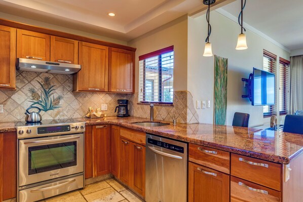 A modern kitchen with wooden cabinets, stainless steel appliances, a granite countertop, and a window with a red valance.