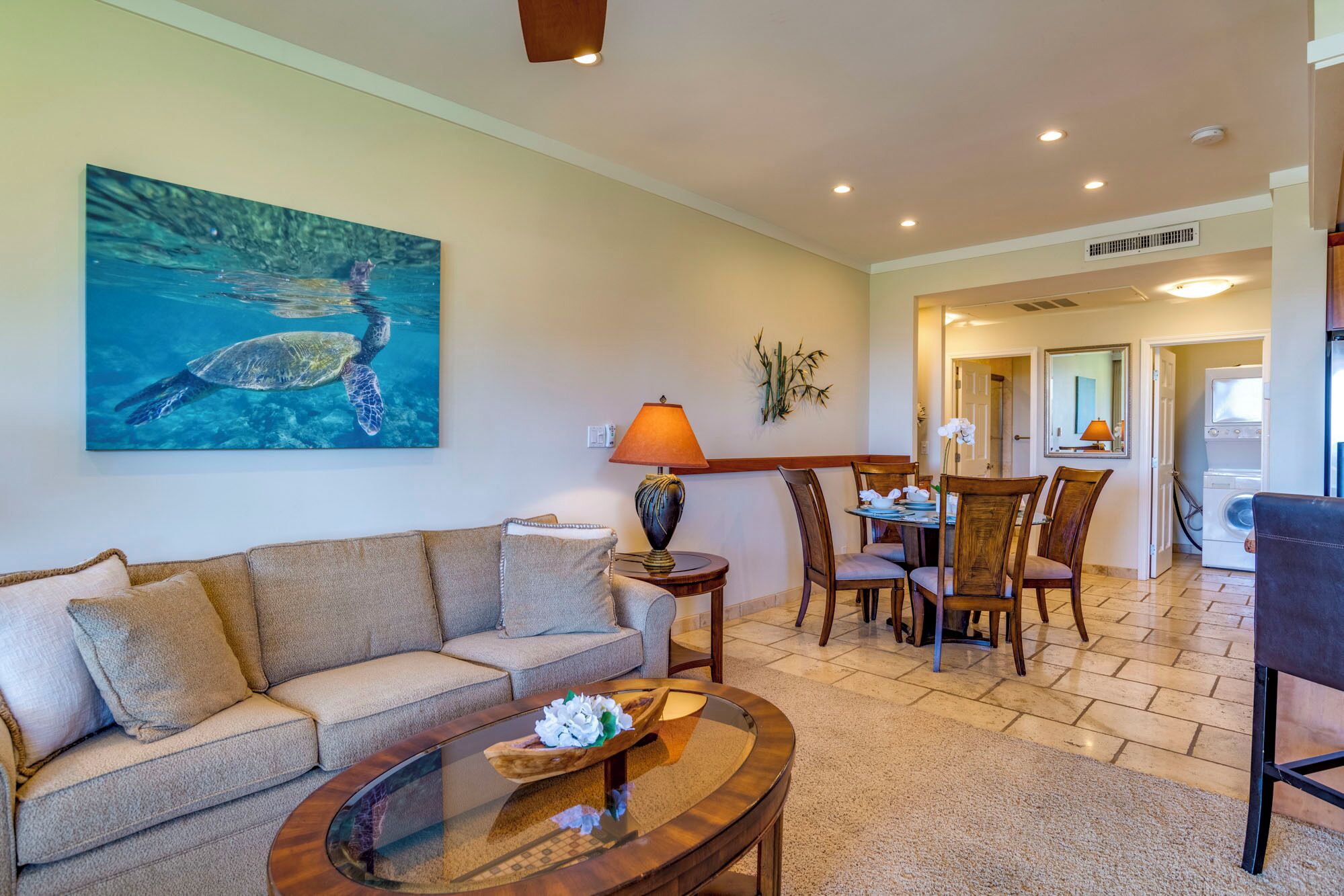 Un salon comprenant un canapé, une table basse et un tableau représentant une tortue de mer. On y trouve également un coin repas avec des chaises et une table.
