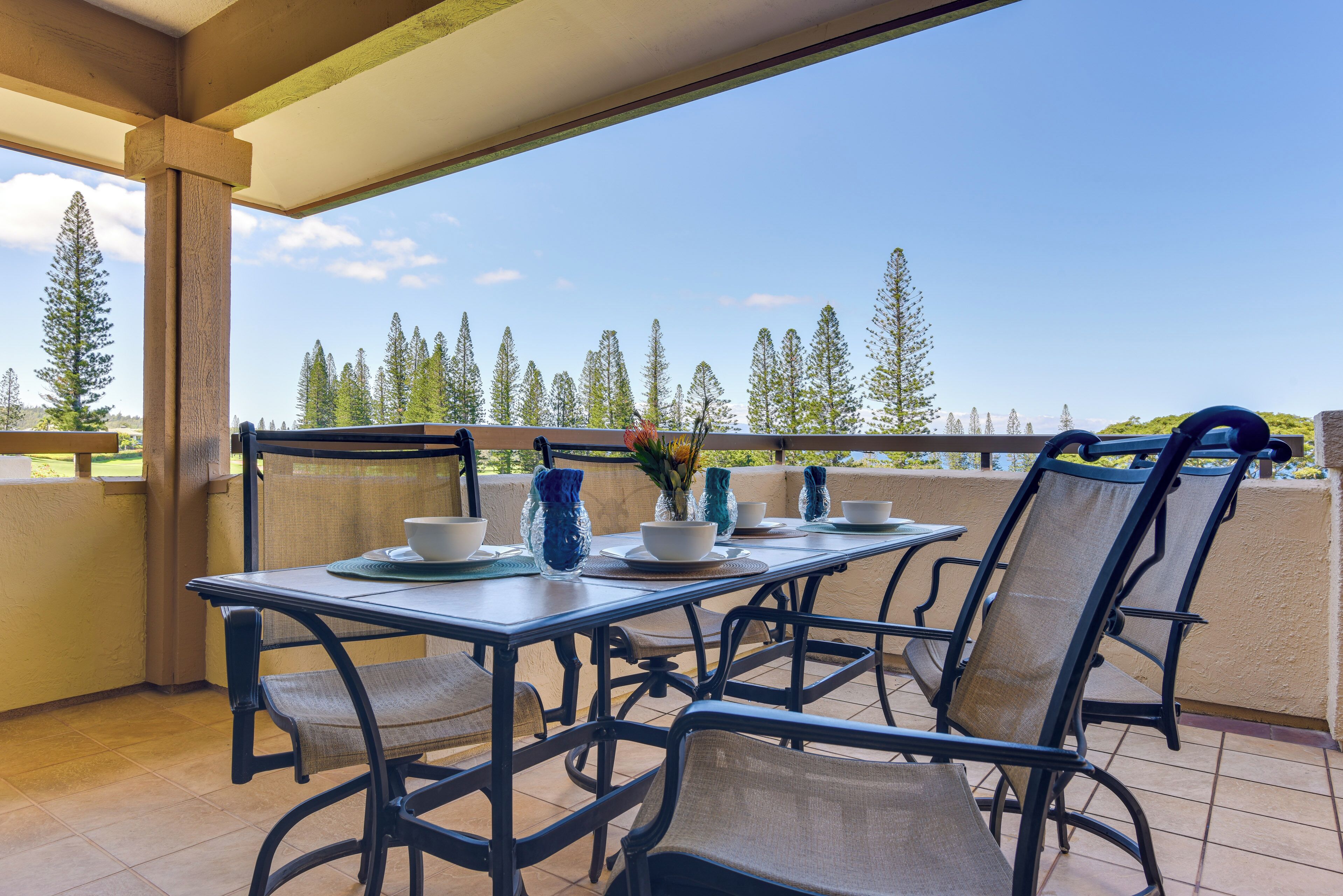 Un área de comedor al aire libre techada con una mesa para dos, sillas y vistas a árboles y un paisaje lejano.