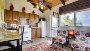 A kitchen with wooden cabinets, a refrigerator, a microwave, and a dining area with a table and chairs. - Charming Kailua-kona Apartment Near Hiking & Golf! (Kailua-Kona)