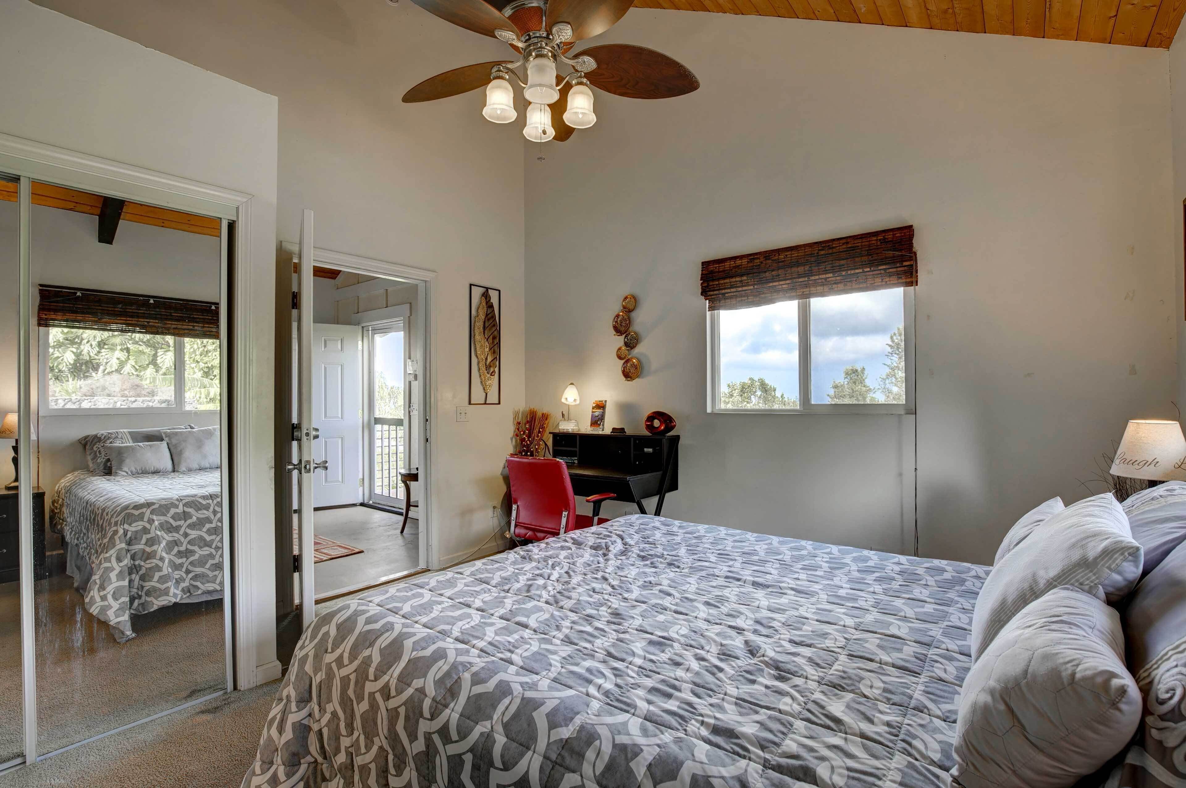 A bedroom with a bed, a desk, a chair, a window with curtains, and a ceiling fan.