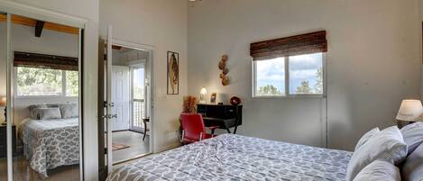A bedroom with a bed, a desk, a chair, a window with curtains, and a ceiling fan.