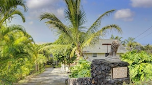 A pathway lined with palm trees leading to a house with a lion statue in front. - Charming Kailua-kona Apartment Near Hiking & Golf! (Kailua-Kona)