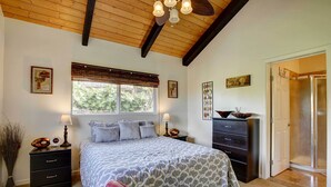 A bedroom with a bed, bedside tables, a dresser, a window with blinds, and a door leading to a bathroom. - Charming Kailua-kona Apartment Near Hiking & Golf! (Kailua-Kona)