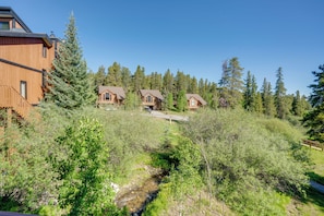 A wooden cabin with a wooden deck, surrounded by dense forest and a small stream. - Ski-in Breck Condo: Walk to Shops & Restaurants! (Breckenridge)