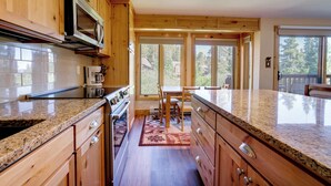 A kitchen with wooden cabinets, granite countertops, a microwave, and a dining area with a table and chairs. - Ski-in Breck Condo: Walk to Shops & Restaurants! (Breckenridge)