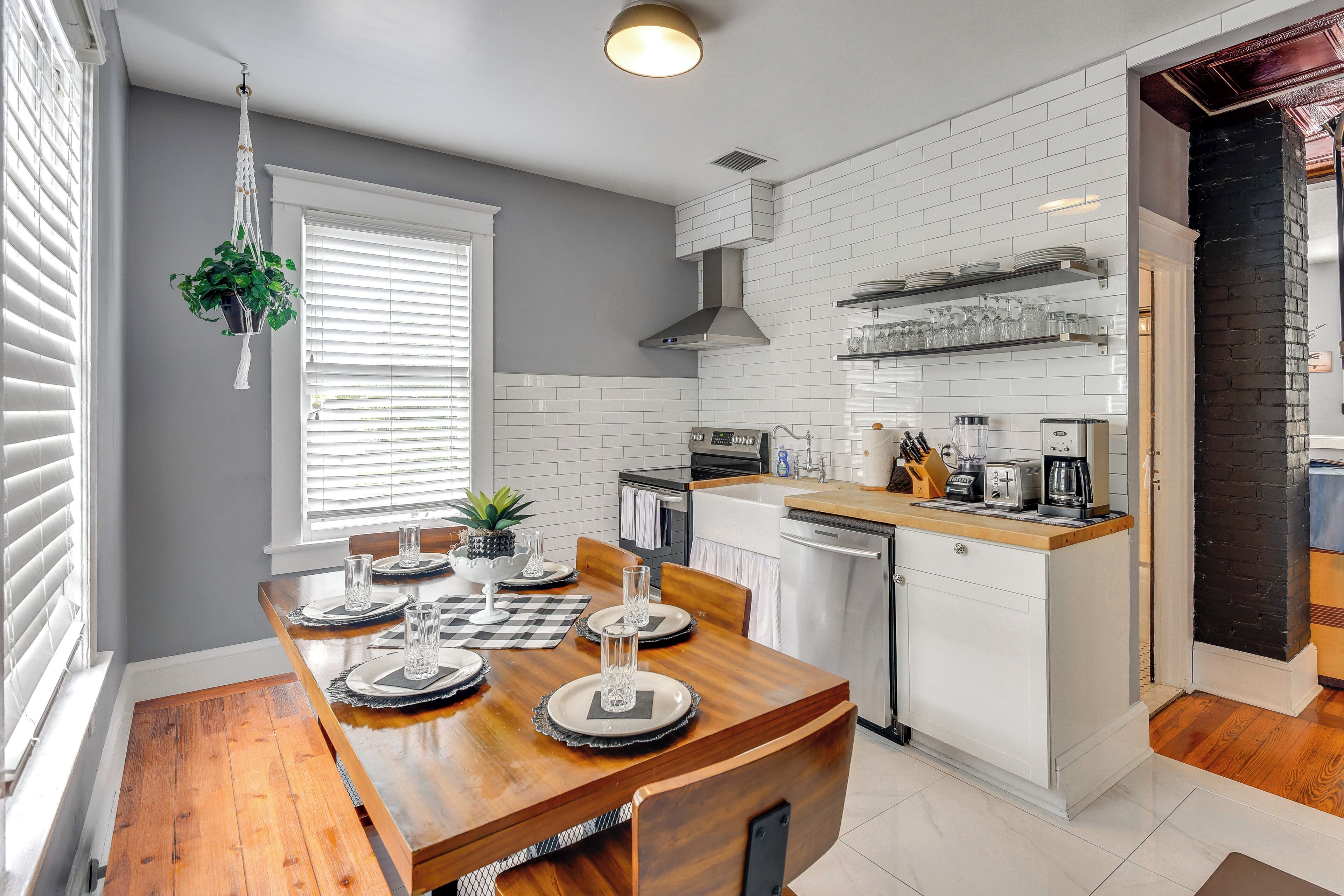 A modern kitchen with white subway tiles, a wooden dining table set for four, and a black brick accent wall.