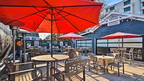 An outdoor patio with tables and chairs, red umbrellas, and a speed limit sign.