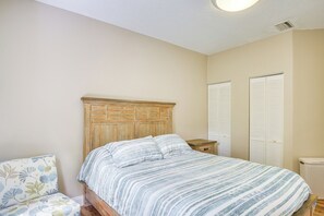 Un dormitorio con cabecera de madera, cama con ropa de cama a rayas, mesita de noche, silla con estampado floral y armario con puertas blancas.