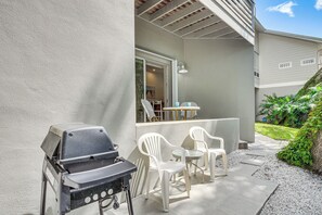 An outdoor patio with a grill, white plastic chairs, and a table. - Walk to the Beach! New Smyrna Hideaway w/ Patio (New Smyrna Beach)