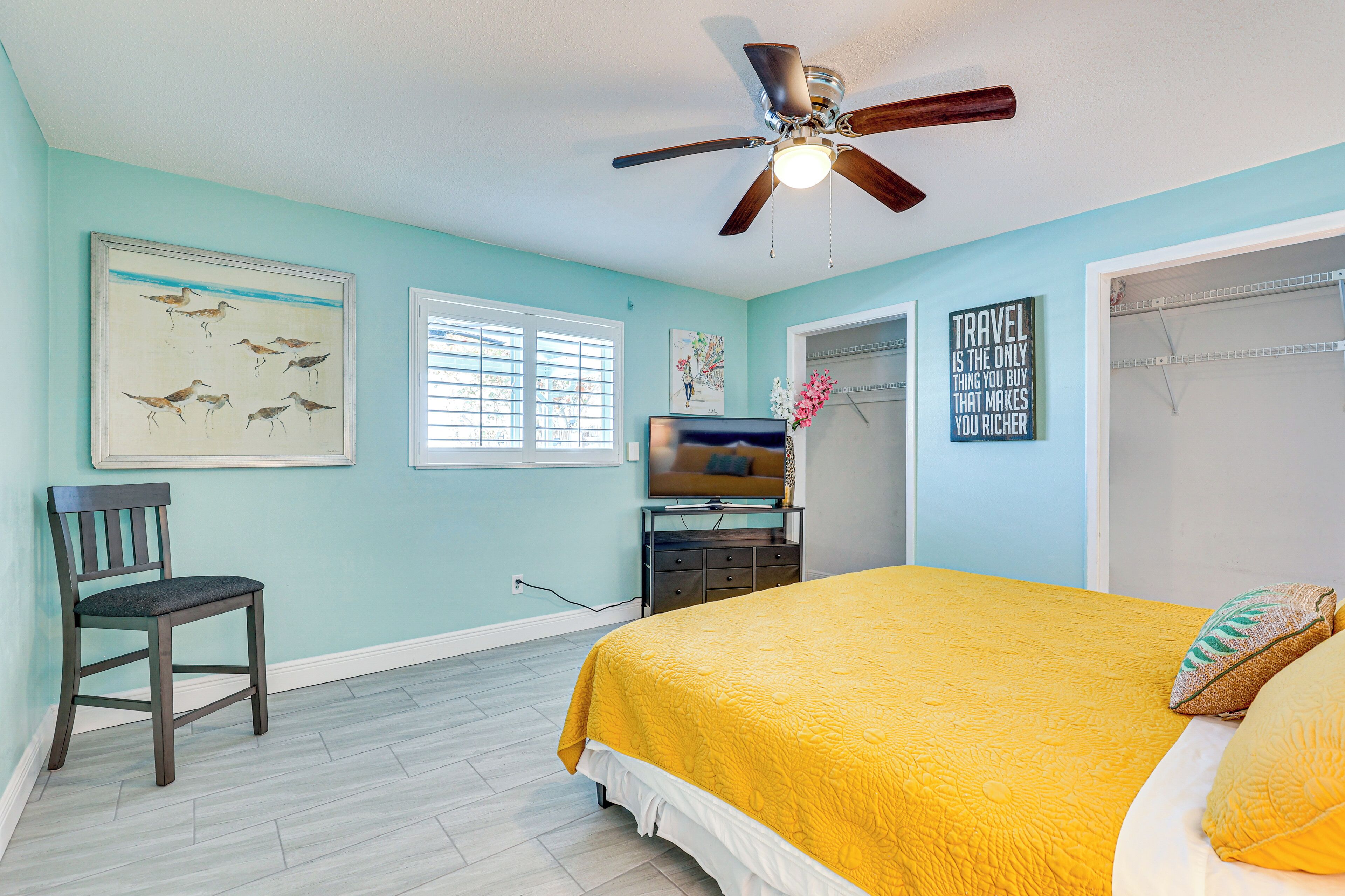 A bedroom with a bed, a chair, a ceiling fan, a television, and artwork on the walls.