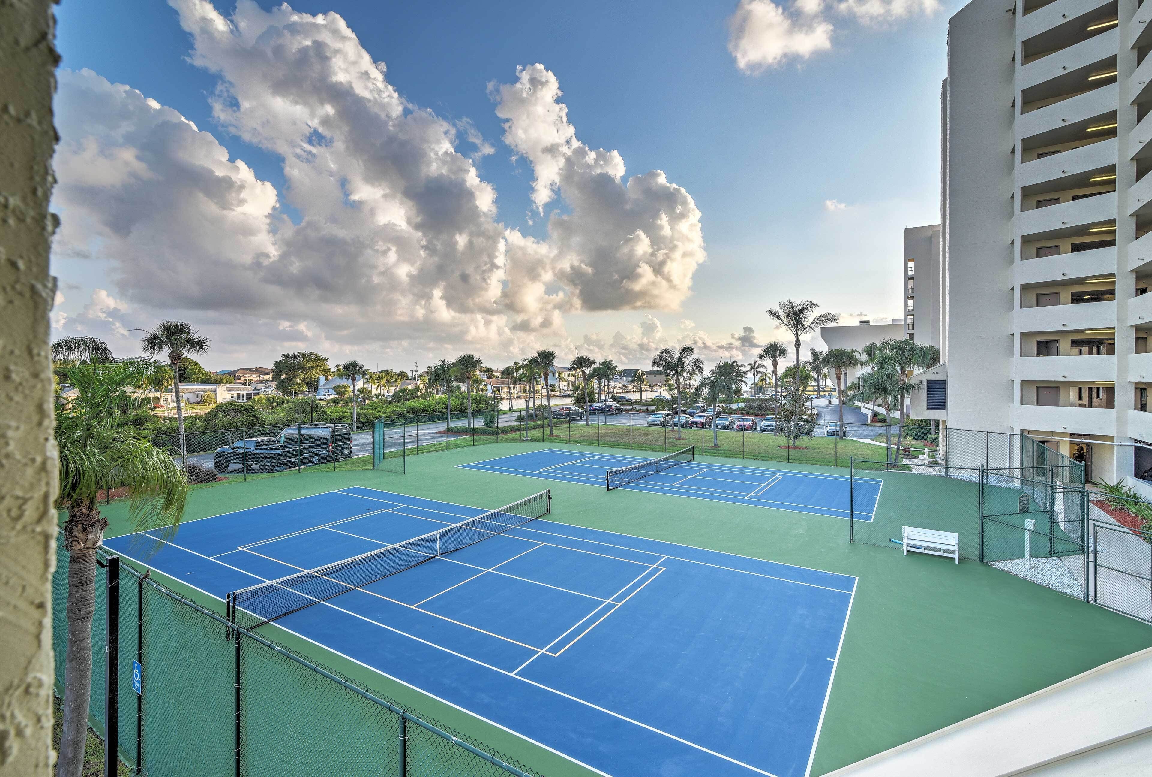 Un court de tennis comprenant plusieurs terrains, entouré d’une clôture, avec un bâtiment en arrière-plan.