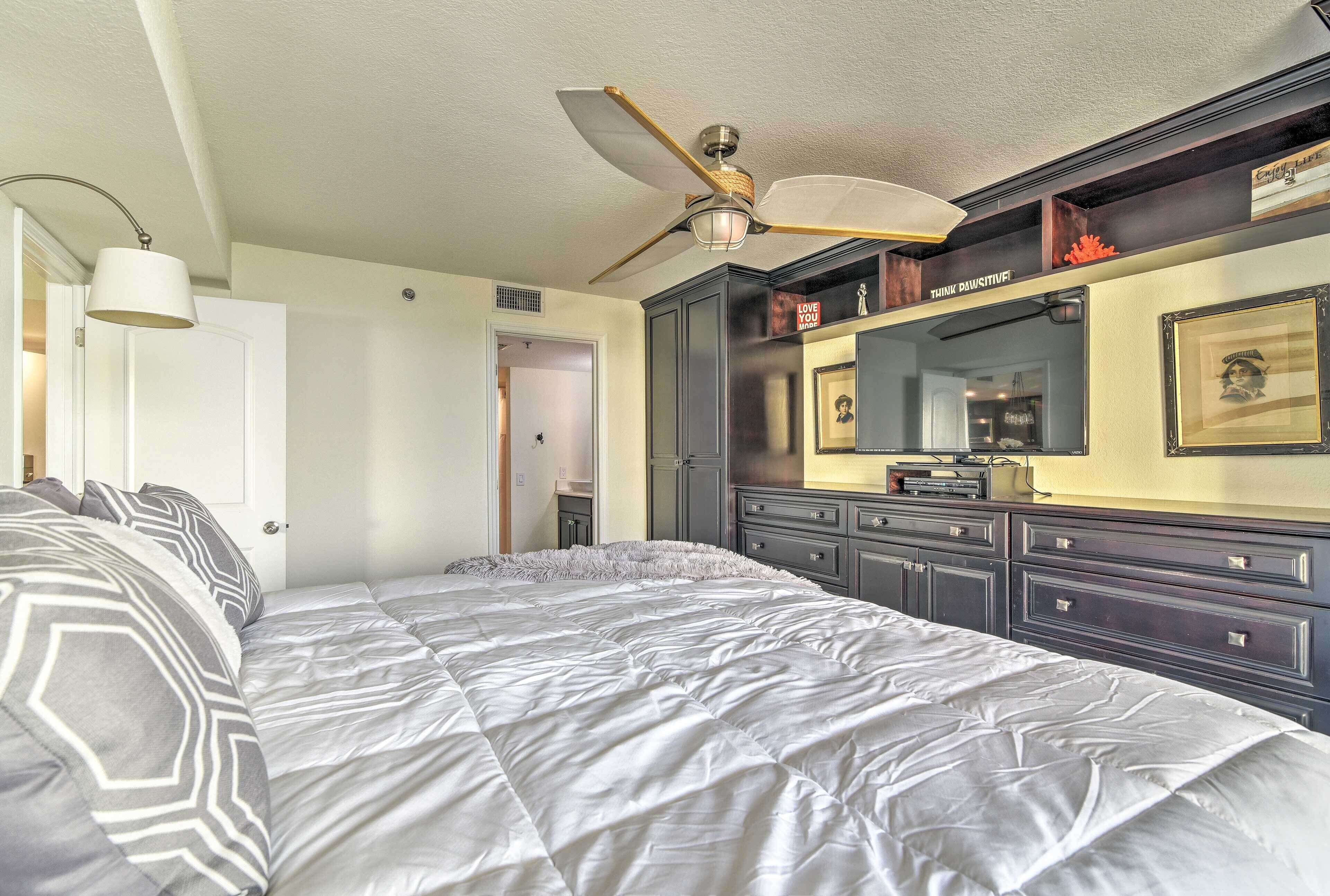 A bedroom with a large bed, a ceiling fan, a dresser, and a mirror.