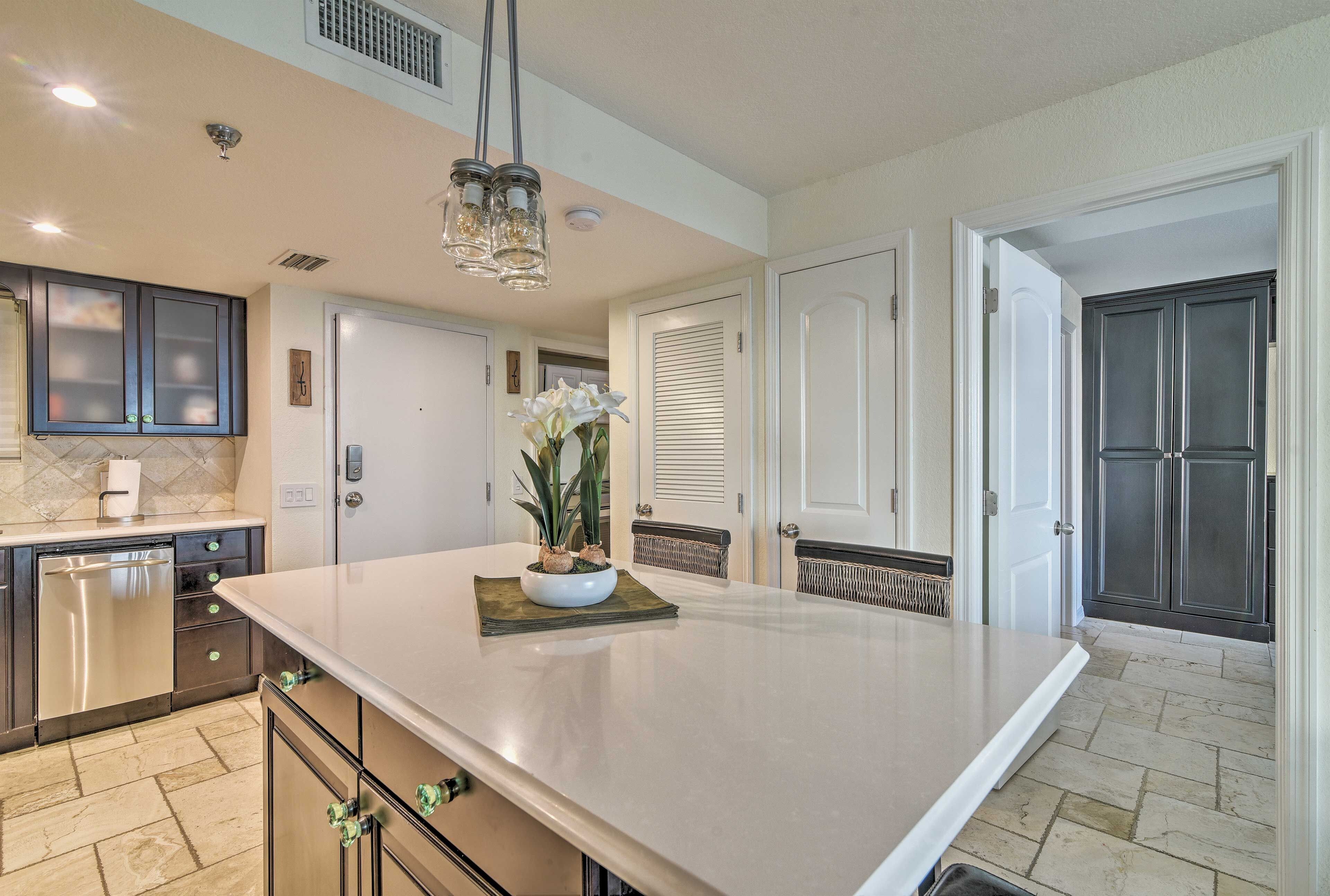 A modern kitchen with a large island, dark cabinetry, and a built-in dishwasher.