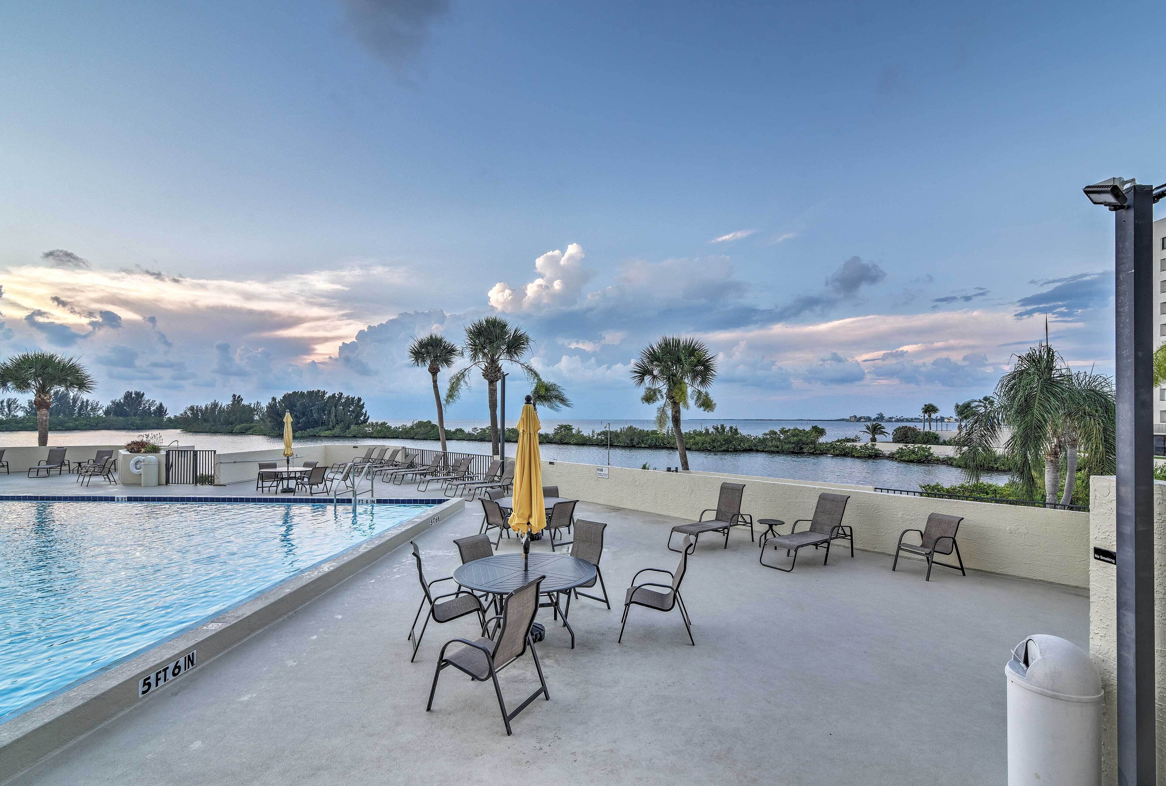 Un espace aménagé au bord de la piscine, avec des chaises longues et des parasols, offrant une vue sur une étendue d’eau bordée de palmiers et sous un ciel dégagé.