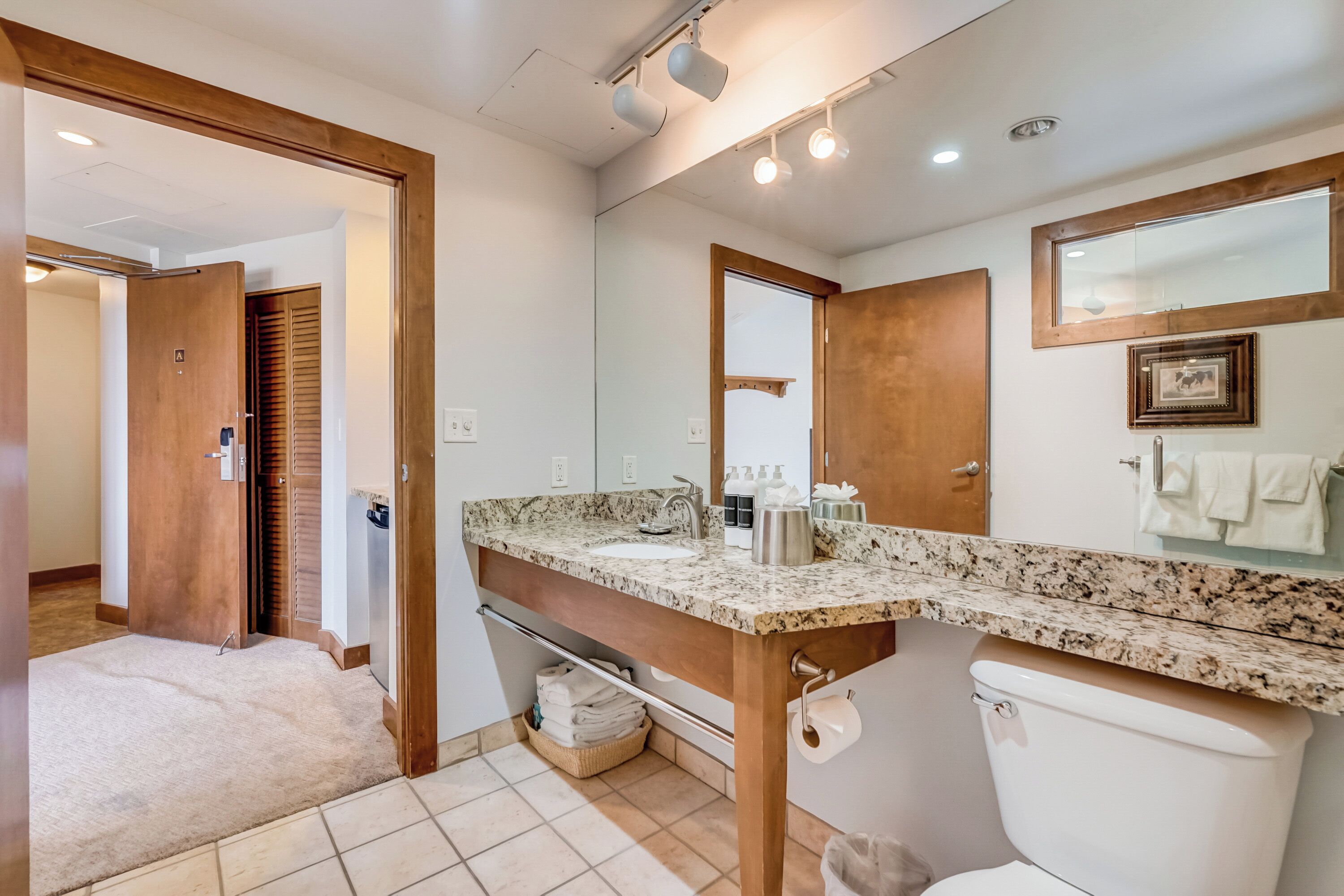 A bathroom with a granite countertop, a sink, a toilet, a mirror, and a towel rack.