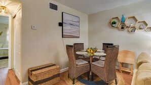 A dining area with wicker chairs, a round glass table, and a wall-mounted hexagonal shelf with decorative items. - Largo Vacation Rental Home w/ Large Yard! (Largo)