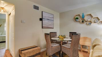A dining area with wicker chairs, a round glass table, and a wall-mounted hexagonal shelf with decorative items.
