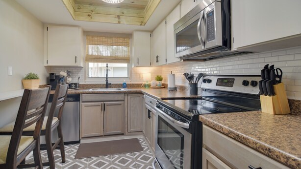 A modern kitchen with wooden ceiling beams, a built-in microwave, stainless steel appliances, and a granite countertop. - Largo Vacation Rental Home w/ Large Yard! (Largo)