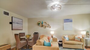 A living room with a dining area, a beige sofa, a patterned rug, and wall-mounted decorations. - Largo Vacation Rental Home w/ Large Yard! (Largo)