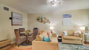 A living room with a dining area, a beige sofa, a patterned rug, and wall-mounted decorations.