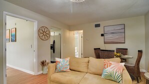 A living room with a beige sofa, a dining area with wicker chairs, and a wall-mounted painting. - Largo Vacation Rental Home w/ Large Yard! (Largo)