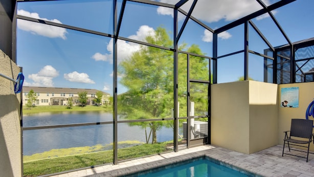 A swimming pool with a glass enclosure, a chair, and a view of a lake and buildings. - ~ 4 Mi to Disney: Compass Bay Resort Gem w/ Views (Kissimmee)