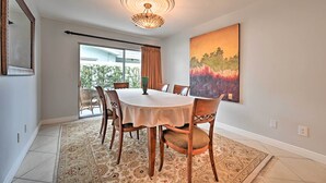 Un espace repas comprenant une table ronde, des chaises, un lustre, un grand tableau et une vue sur l’extérieur, visible à travers une porte vitrée.