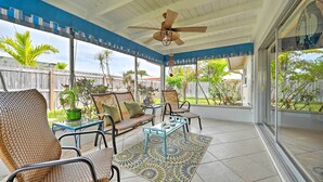 Un patio couvert aménagé avec des meubles en osier, un ventilateur de plafond et un tapis à motifs.