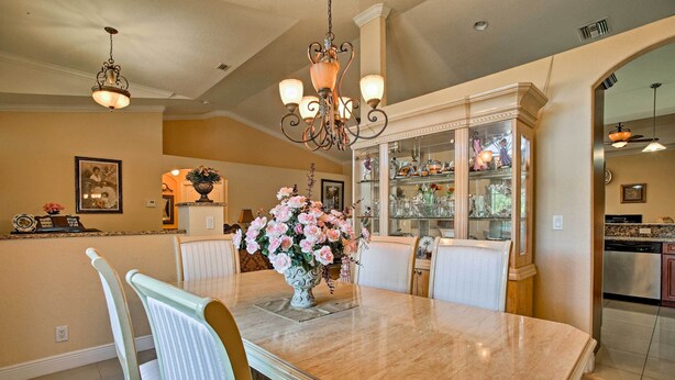 A dining area with a marble table, white chairs, a chandelier, and a glass cabinet with decorative items.